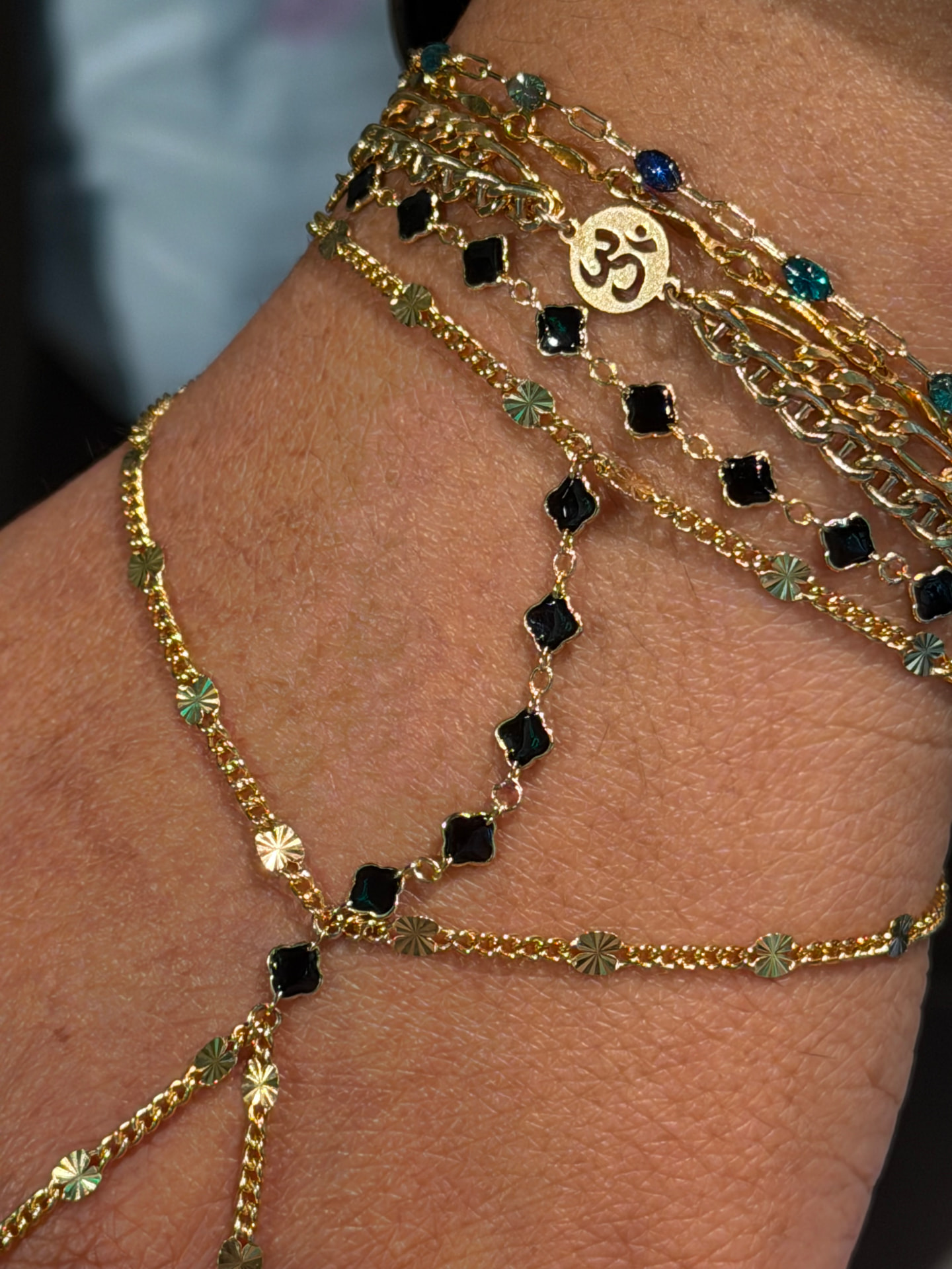 Layered gold permanent bracelets with black clover accents