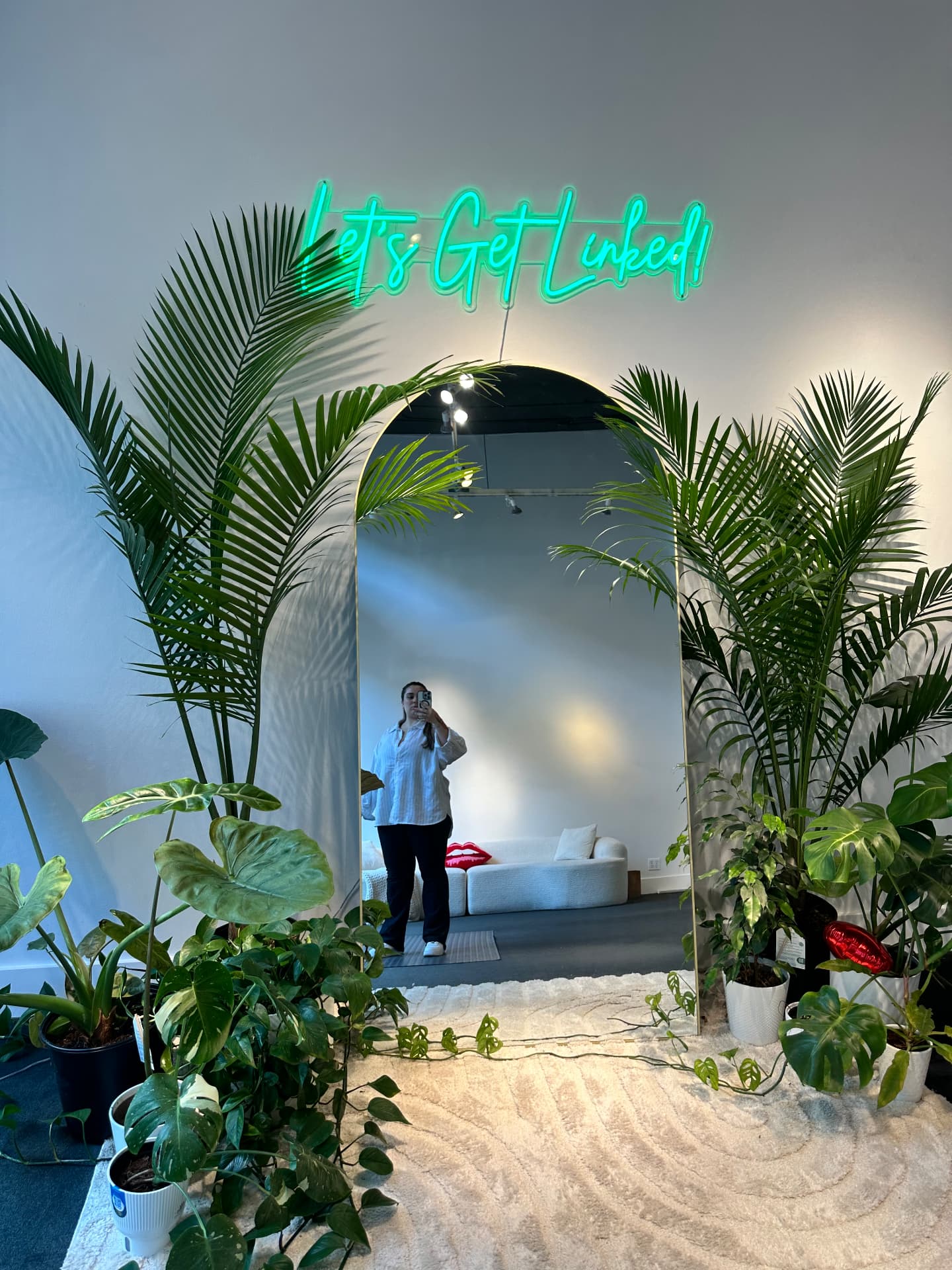 Studio entry mirror with Let's Get Linked neon sign and plants
